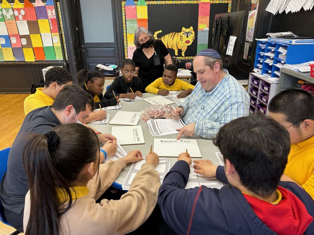 A teacher sits down in a semi circle with his special education elementary students to complete a SnackTime Explorers lesson. 