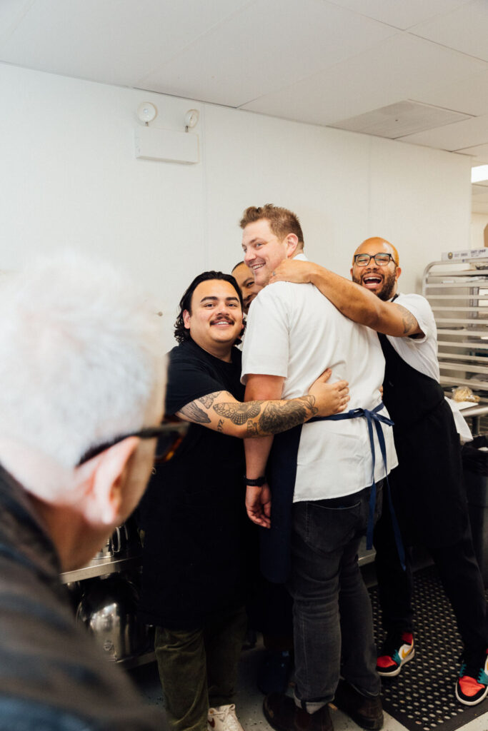 Gala guest chefs Jonathan Zaragoza, Tim Flores, Joe Flamm, and James Martin hug it out in the kitchen at the 2023 Feed Your Mind gala. 