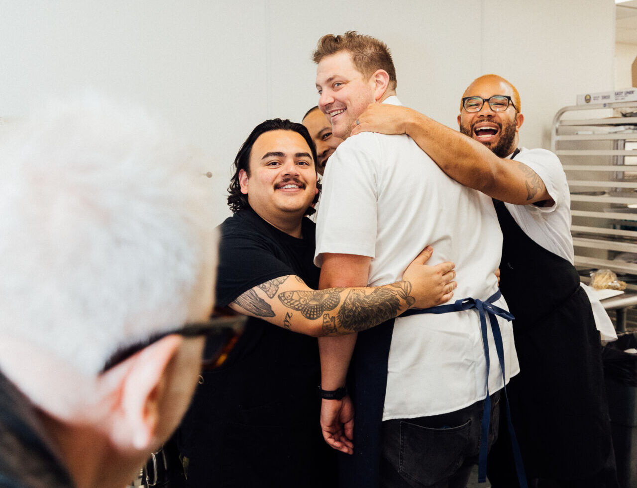 Gala guest chefs Jonathan Zaragoza, Tim Flores, Joe Flamm, and James Martin hug it out in the kitchen at the 2023 Feed Your Mind gala.