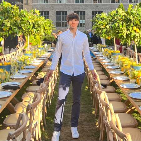 Pilot Light Intern Kai Fogelson smiles at the camera in between two long outdoor dinner tables.
