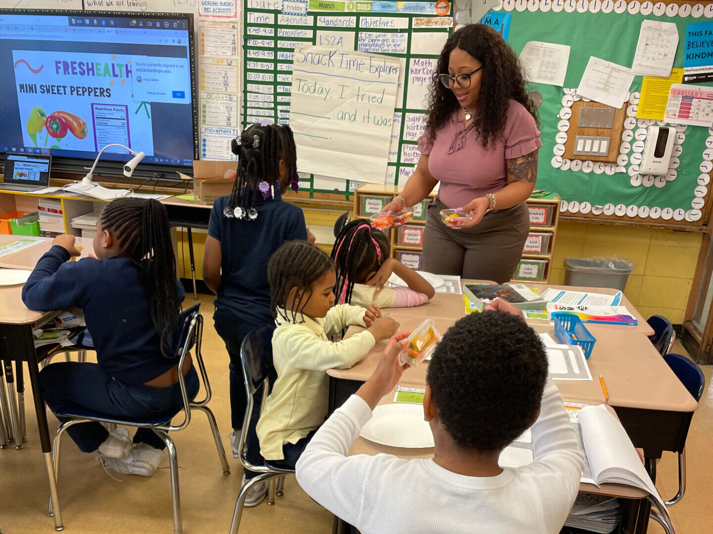 An elementary school teacher hands out sweet pepper FFVP snacks to her room of SnackTime Explorers students.